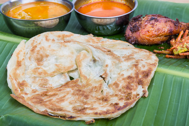 Roti prata or fried flatbread with curries, condiments and chicken